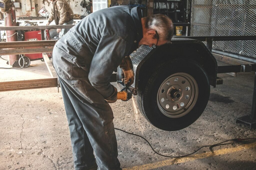 A person crouched at the hitch of a travel trailer checking the coupler and safety chains